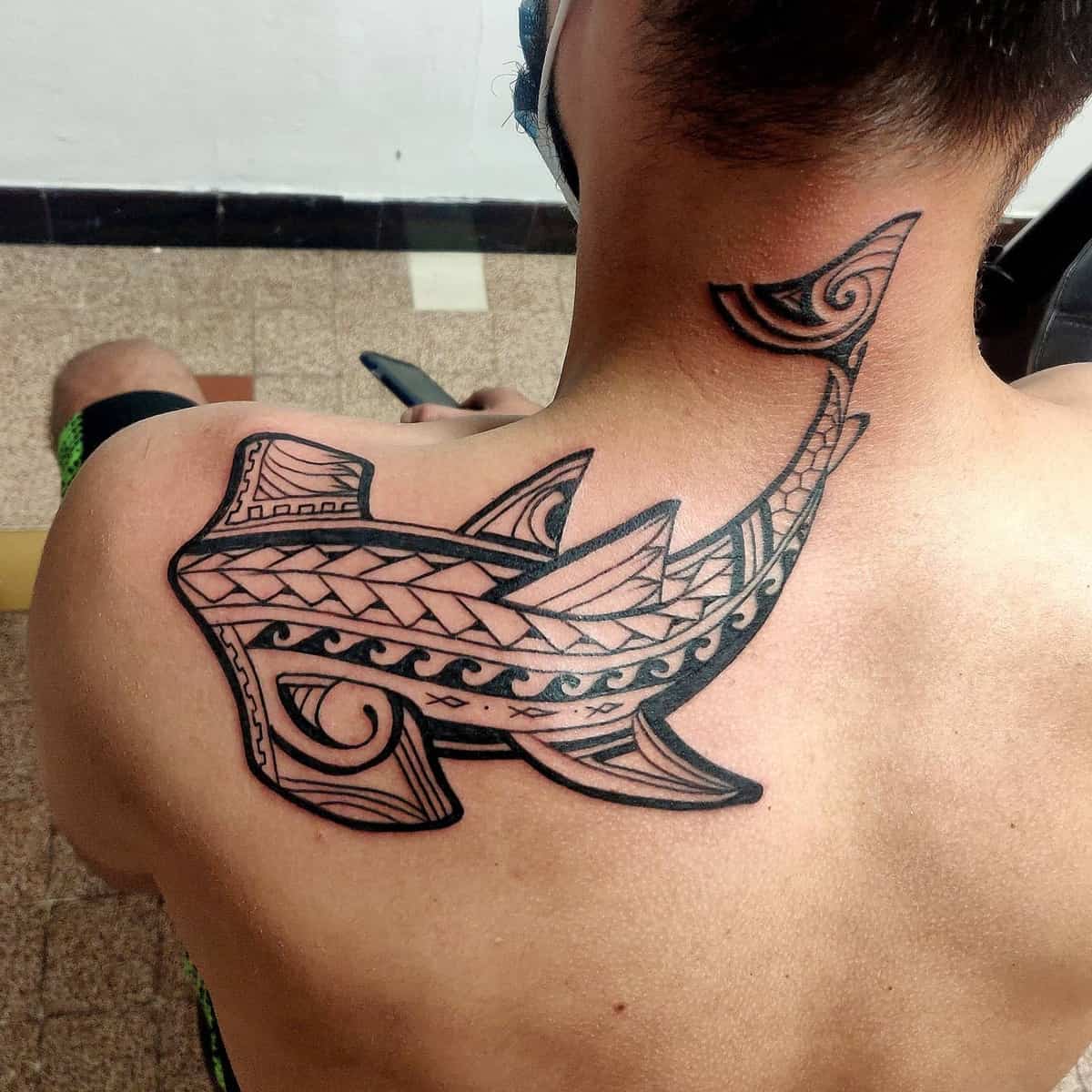 A Polynesian tribal-style shark tattoo on their upper back