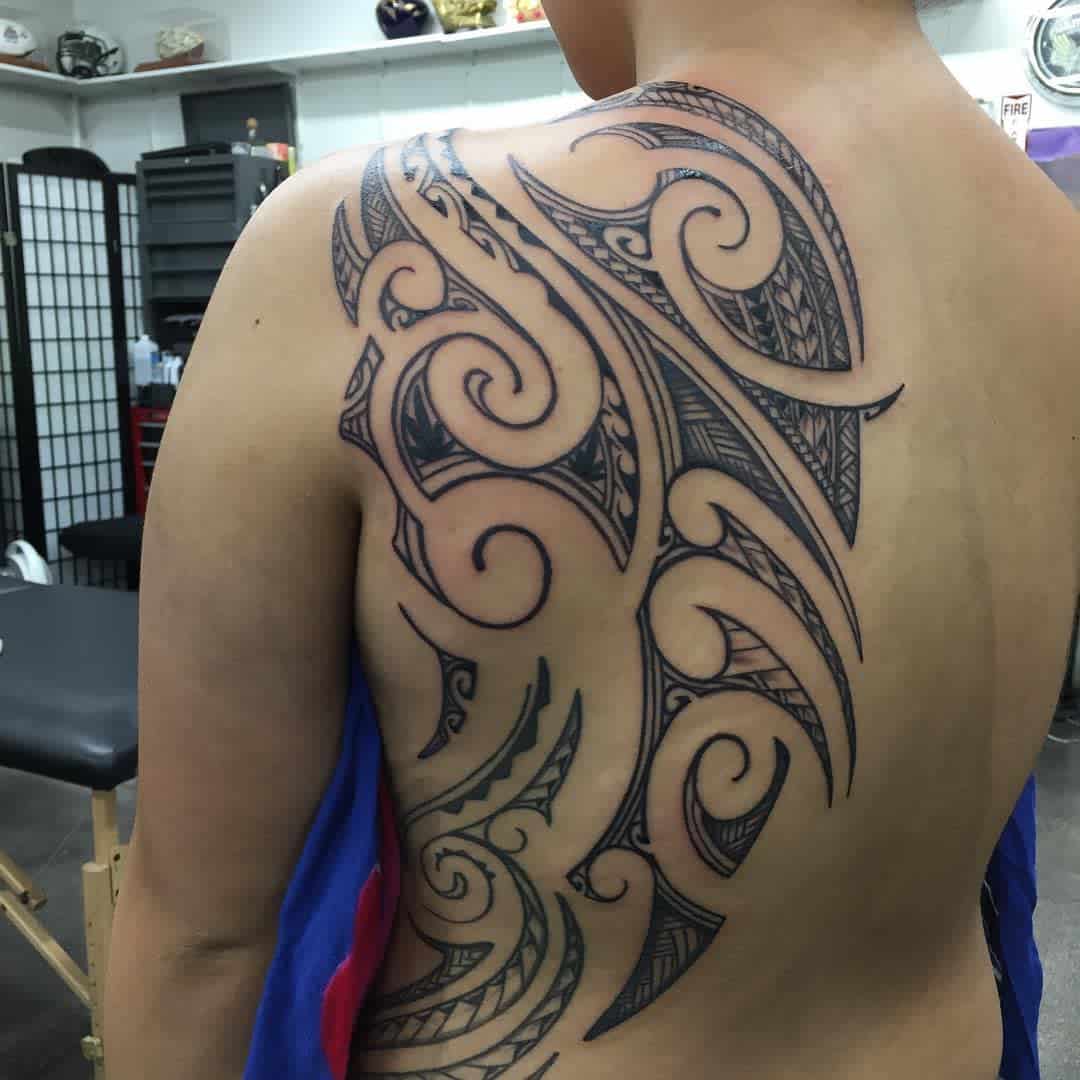A bold, intricate Polynesian tribal tattoo covers the upper back, featuring swirling and geometric patterns