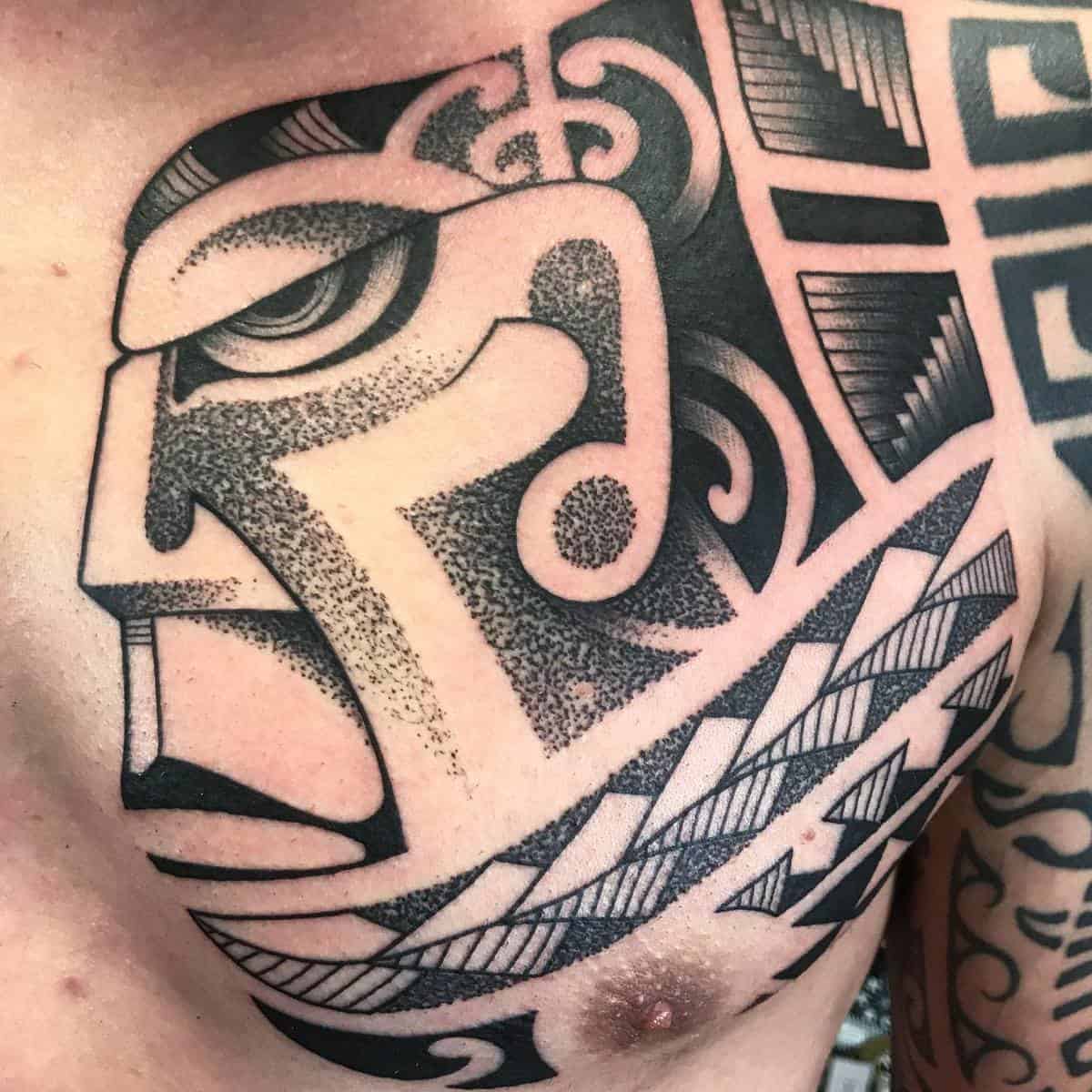 Close-up of a detailed Polynesian tribal tattoo depicting an abstract face design on a chest