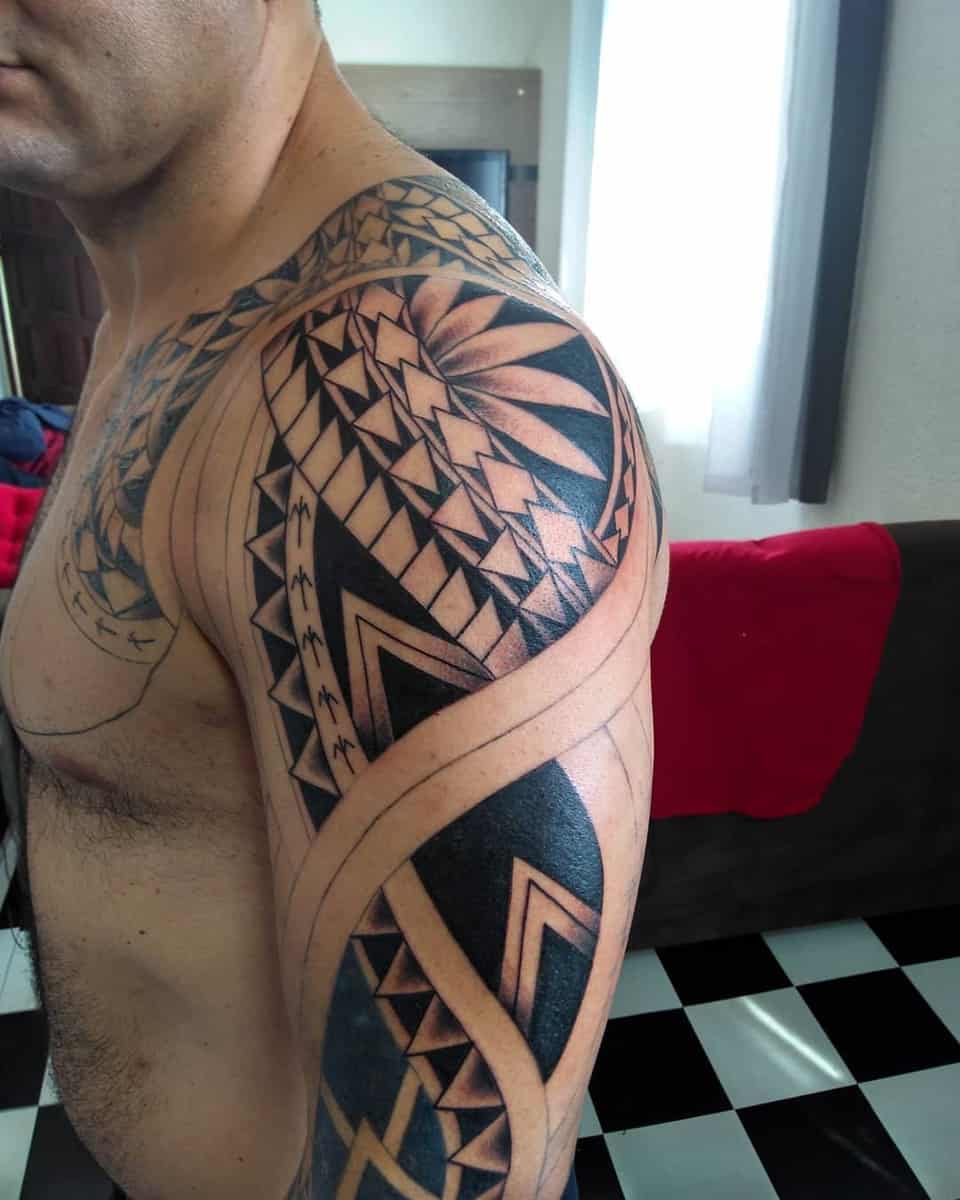 A tattoo sleeve with intricate black geometric patterns and Polynesian designs on an upper arm and shoulder, viewed from a side angle