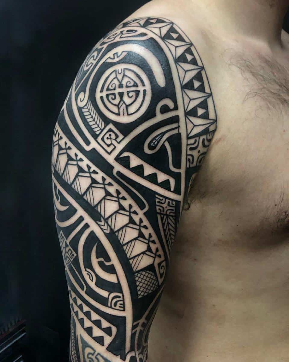 A shirtless man displays an intricate Polynesian black geometric and tribal tattoo sleeve on his right arm and chest