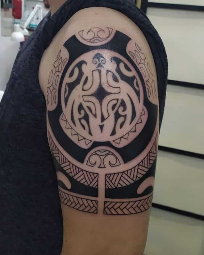 A large, intricate tribal tattoo featuring bold black patterns and designs on an upper arm