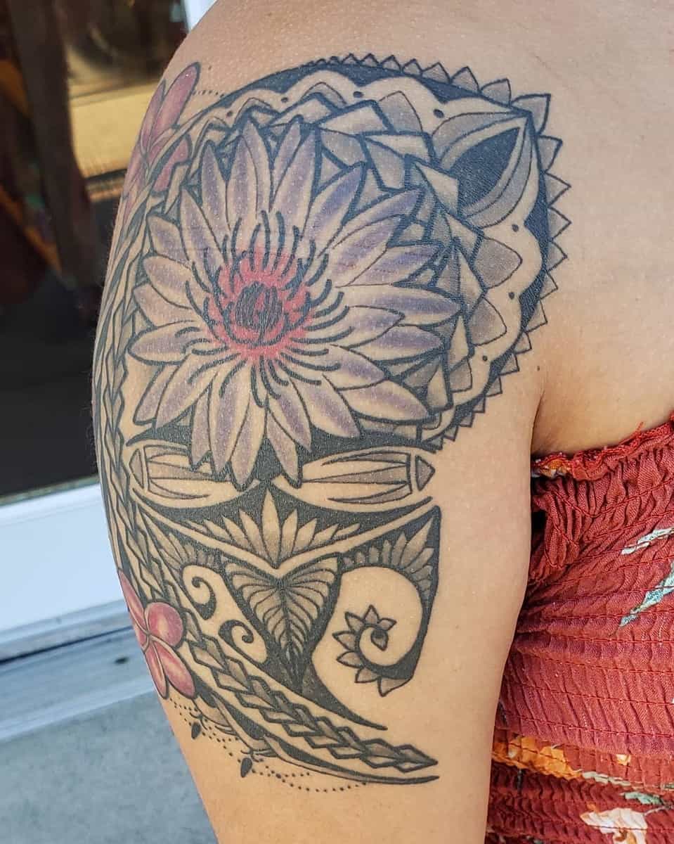 A close-up of a shoulder tattoo featuring a stylized floral design in black and red ink on an upper arm