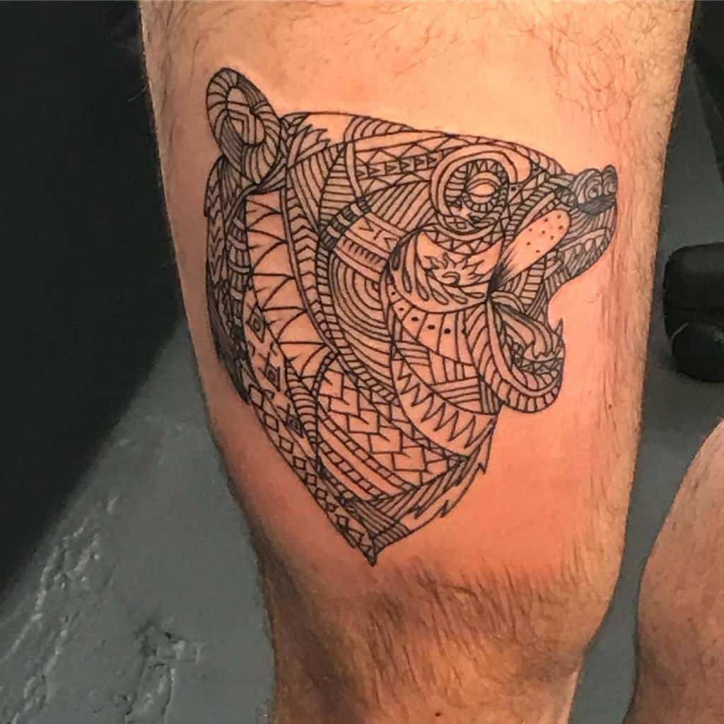 Tattoo of a bear featuring an ornate head adorned with intricate geometric and tribal patterns on a person's thigh