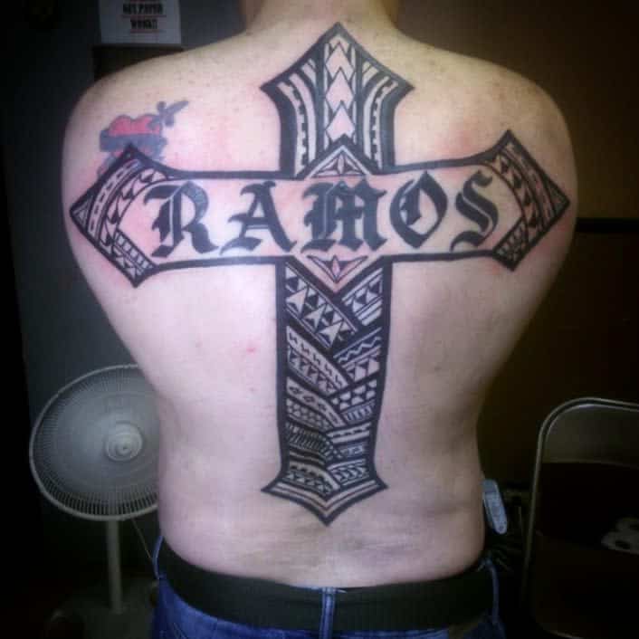 A striking back tattoo features a prominent cross intertwined with tribal Polynesian designs, all anchored by the name "Ramos" in bold letters