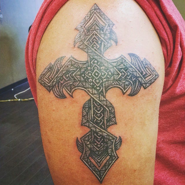 An intricate Polynesian tribal cross tattoo adorns the upper arm
