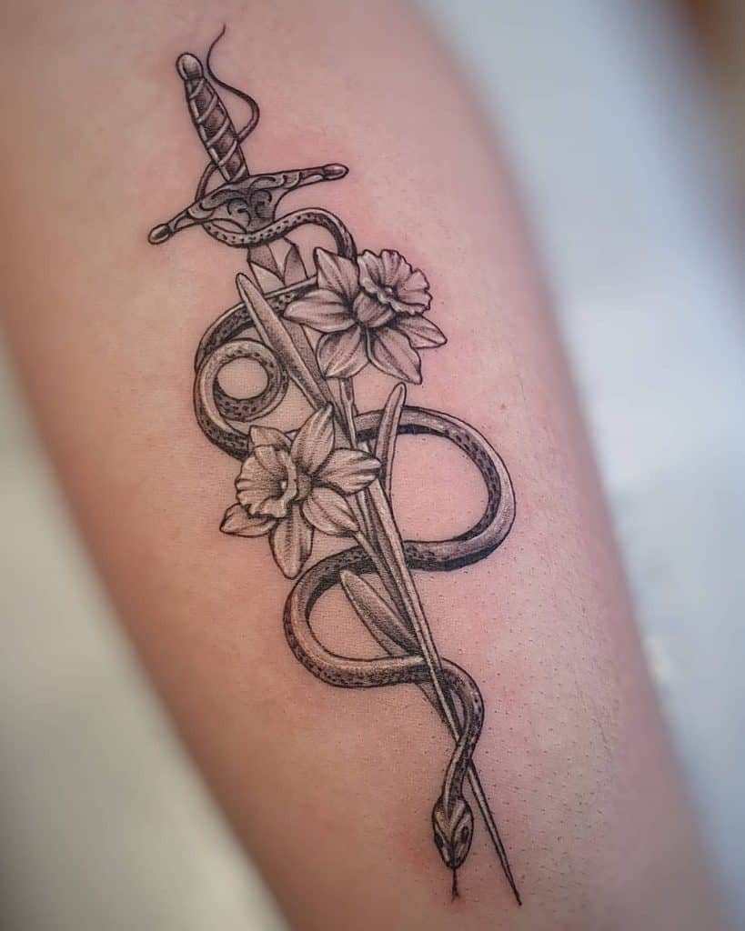 A black-and-white tattoo of a dagger entwined with a snake, surrounded by delicate daffodils, creating a contrast between danger and beauty.