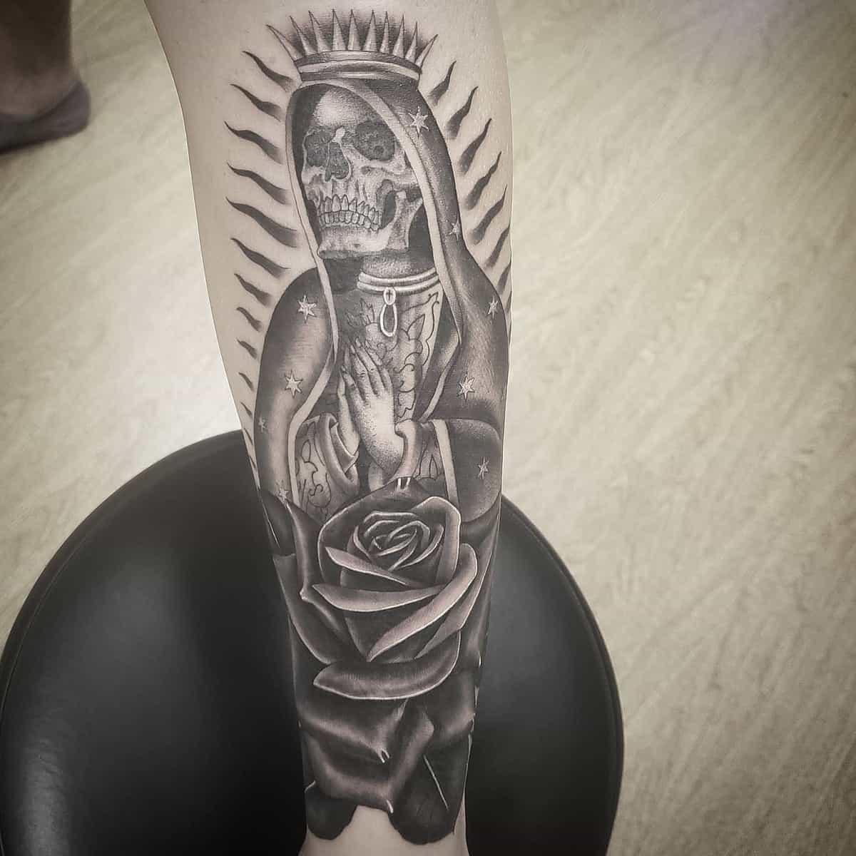 Praying Santa Muerte forearm tattoo, featuring a skeletal figure with radiant lines, adorned with a rose