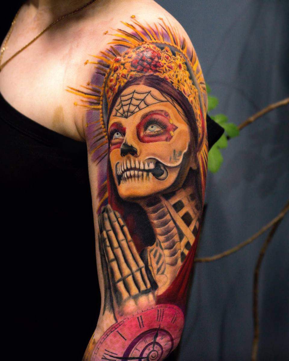 A vibrant Santa Muerte tattoo with bold colors, praying skeleton, crown, and clock details