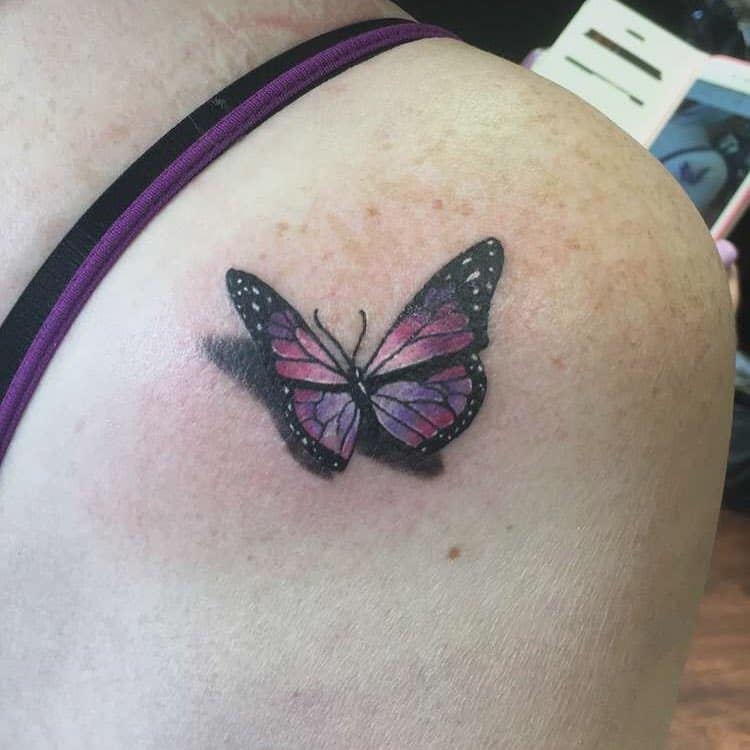 A pink and purple butterfly tattoo on a person's shoulder, with a bit of shadow for depth
