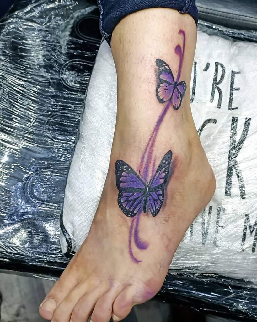 Foot tattoo of two purple butterflies with black outlines and a swirling purple trail
