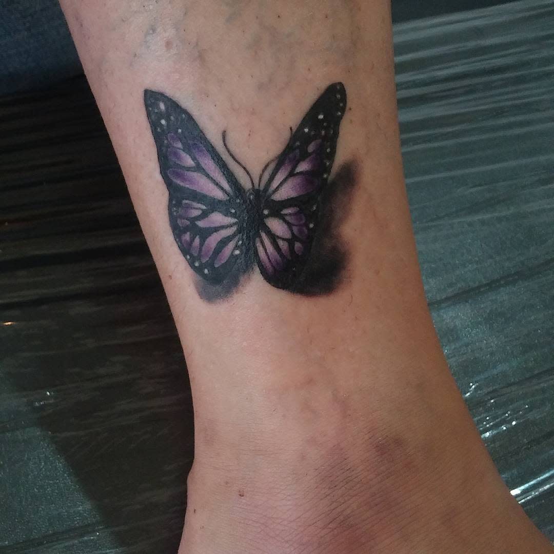 Tattoo of a purple and black butterfly on an ankle