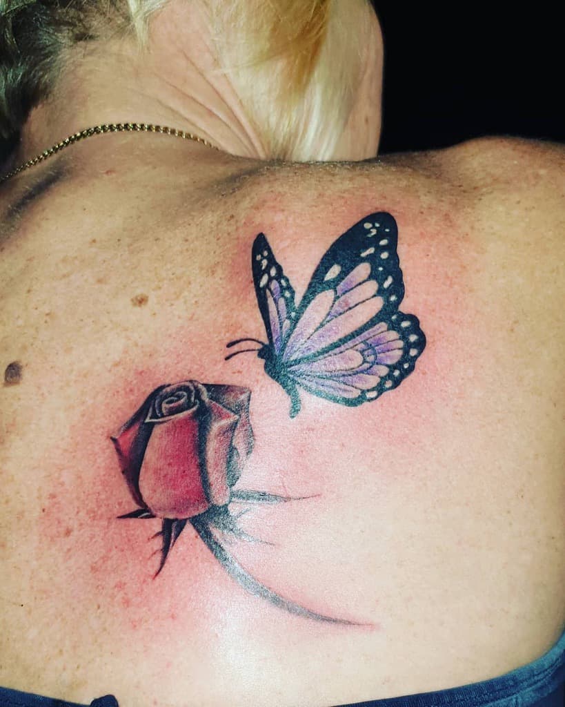 A tattoo of a butterfly above a rose on a woman's upper back