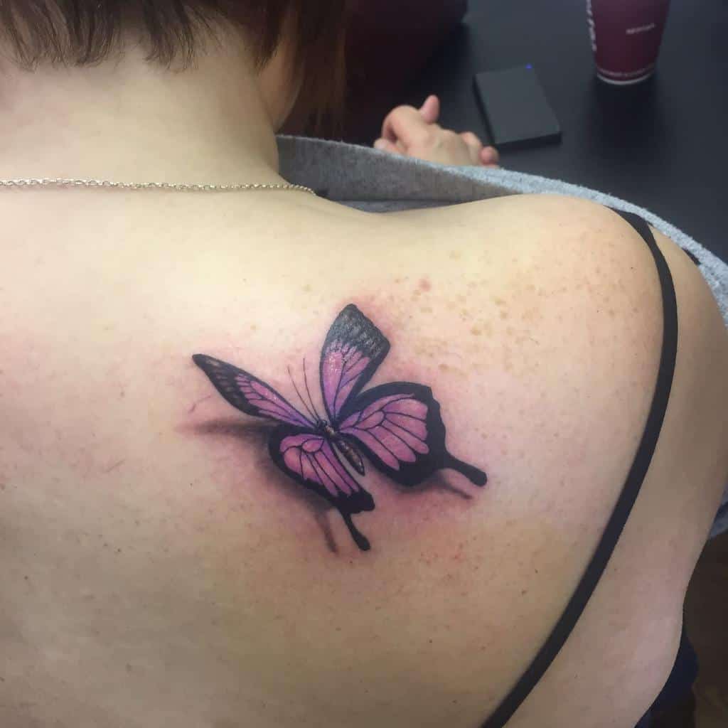 Back tattoo of a pink and black butterfly on a woman's shoulder