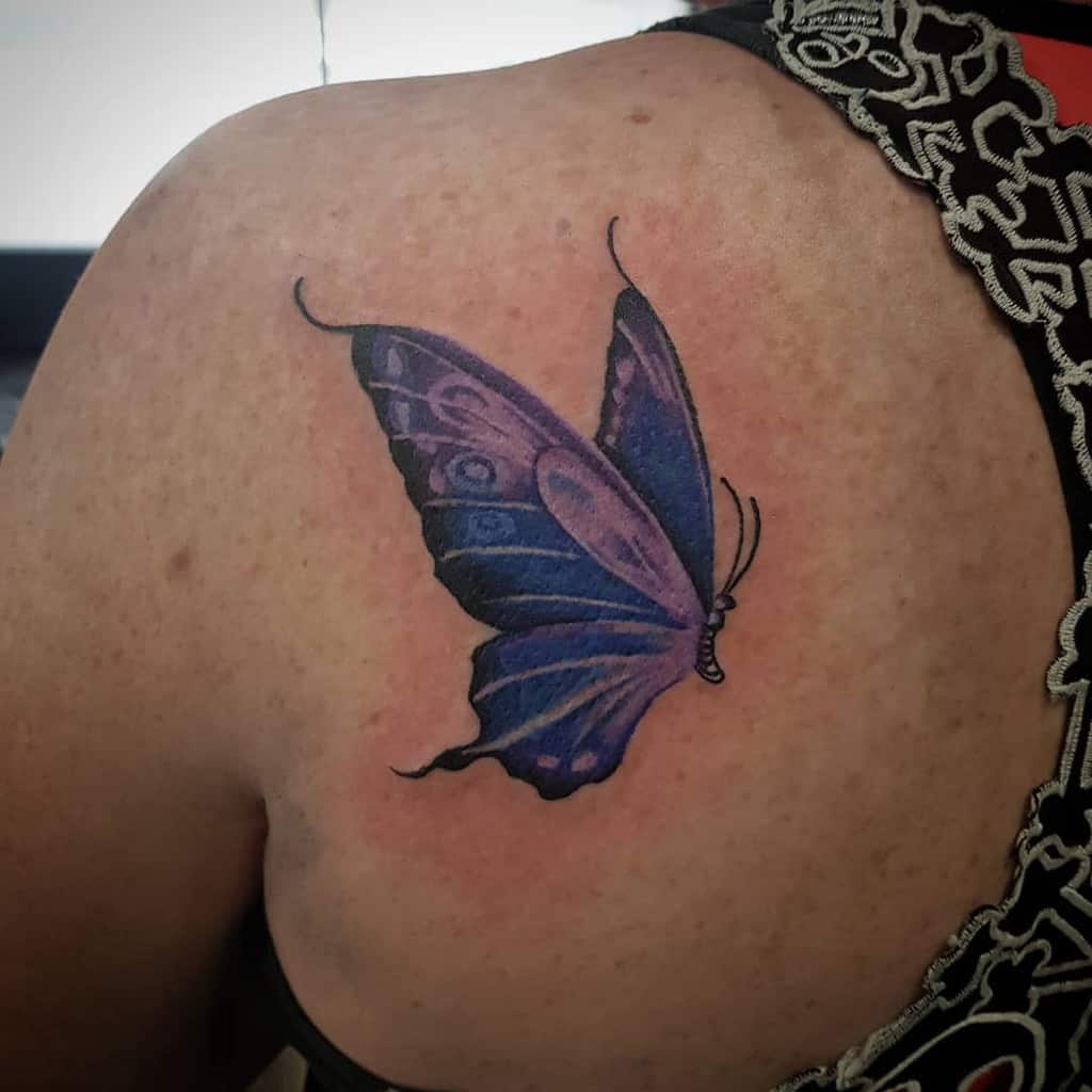 A vibrant purple butterfly tattoo on an upper back