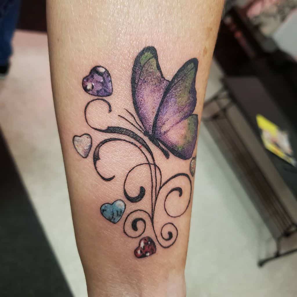 A forearm tattoo with a colorful butterfly, hearts, and swirling patterns