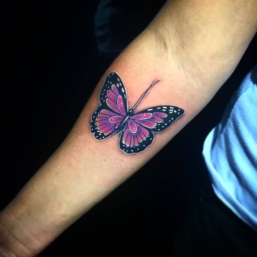 A realistic, purple butterfly tattoo on a forearm