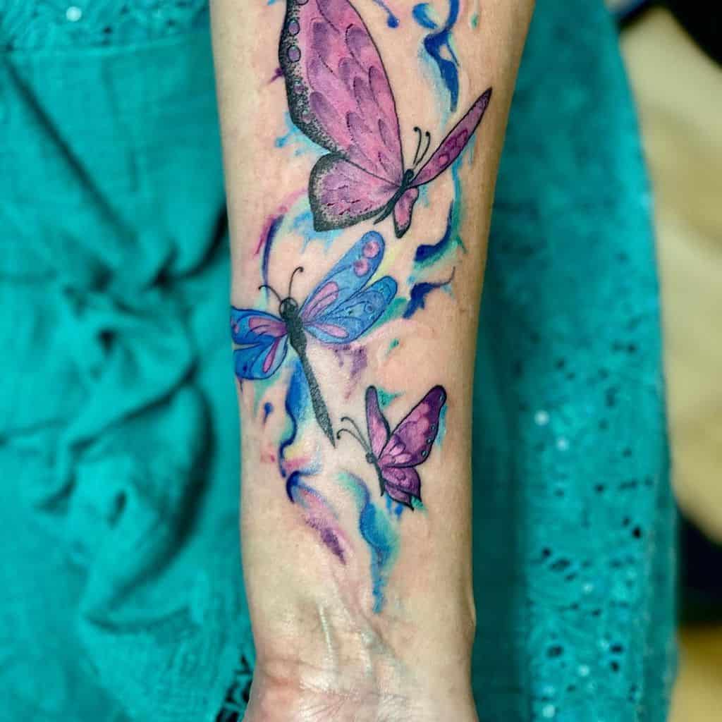 Forearm tattoo featuring three colorful butterflies with a vibrant blue and pink watercolor design