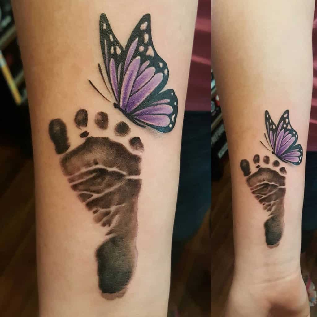 A tattoo of a black footprint with a purple butterfly on an inner forearm