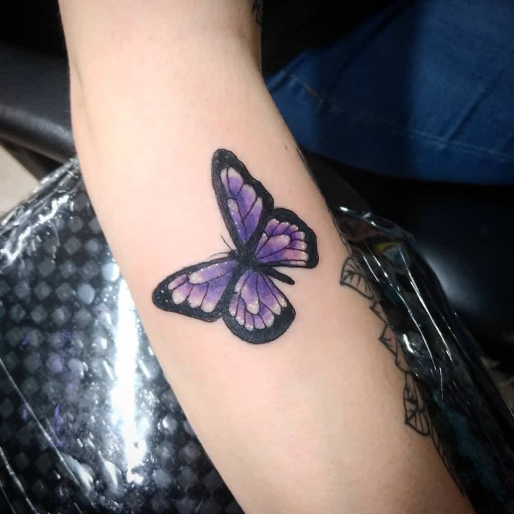 A purple and black butterfly tattoo on an inner forearm