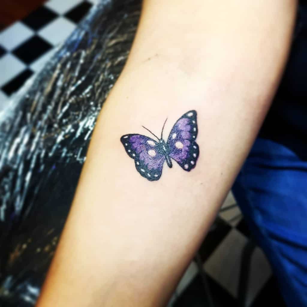 A forearm with a purple and black butterfly tattoo with white spots