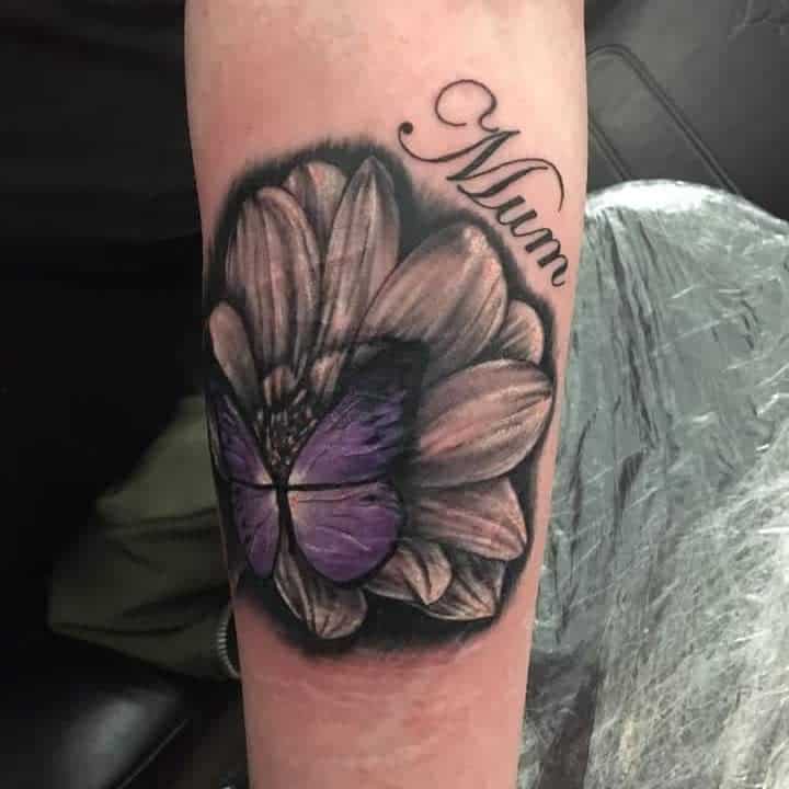 Tattoo of a flower with a purple butterfly in the center and the word "Mum" above it