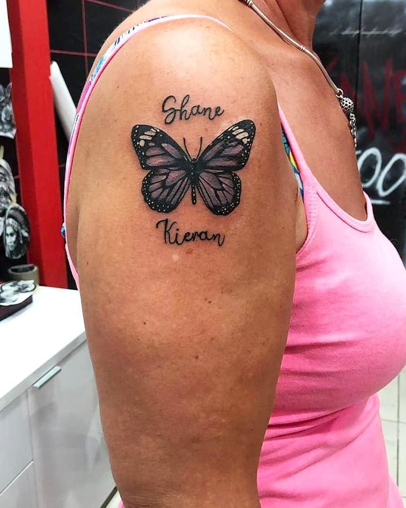 A tattoo of a purple butterfly with the names "Shane" and "Kieran" on a woman's upper arm