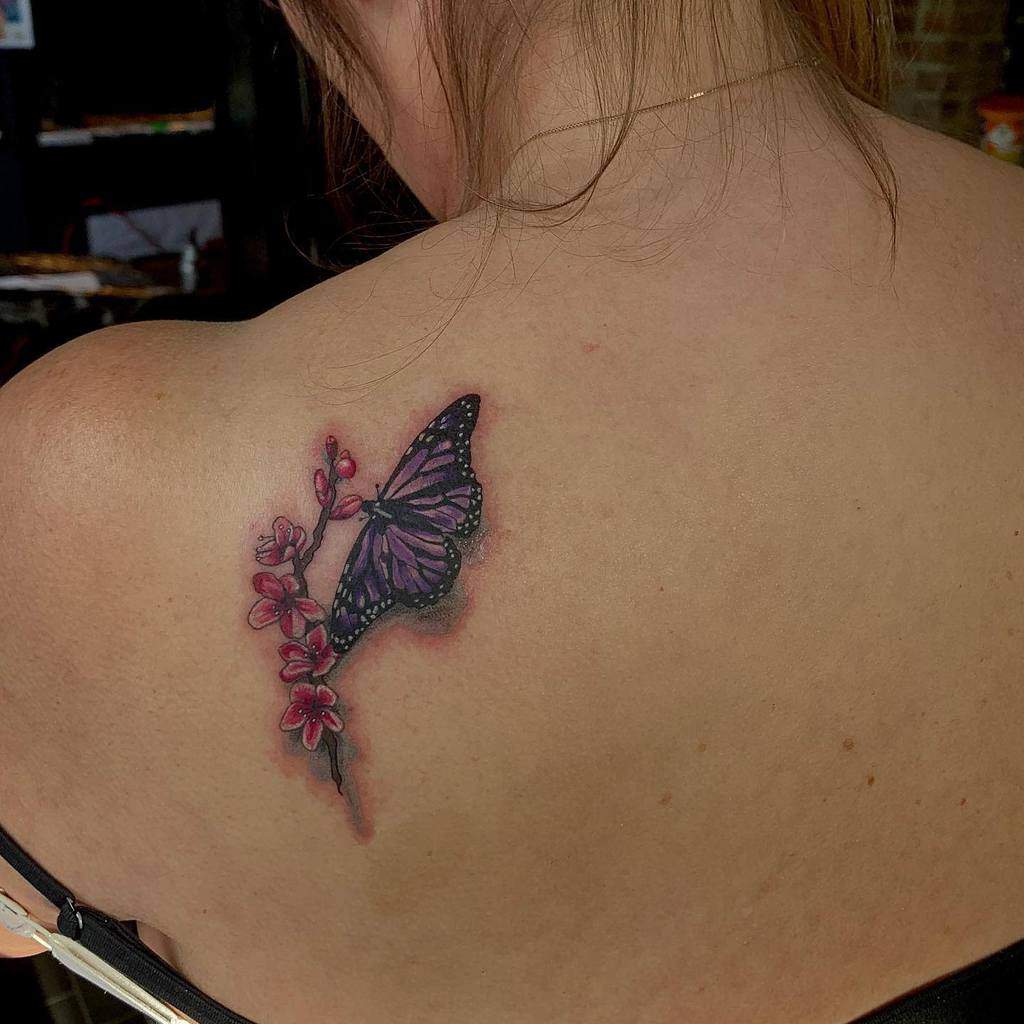 Shoulder tattoo showing a purple butterfly perched on pink cherry blossoms