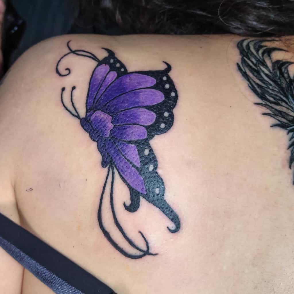A tattoo of a purple butterfly with black details on an upper back