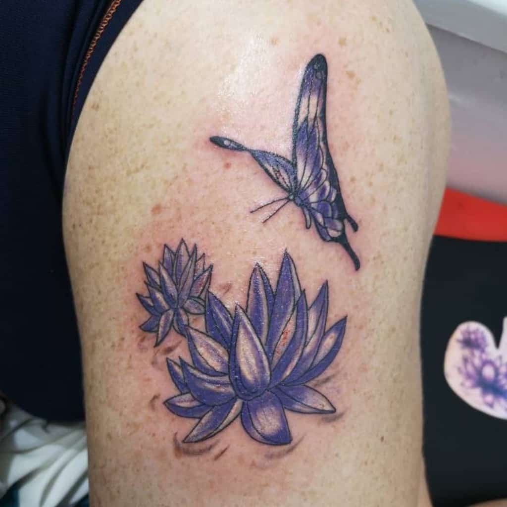 A tattoo of a purple butterfly and two lotus flowers on a shoulder