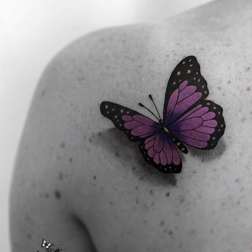 Purple and black butterfly tattoo on a shoulder