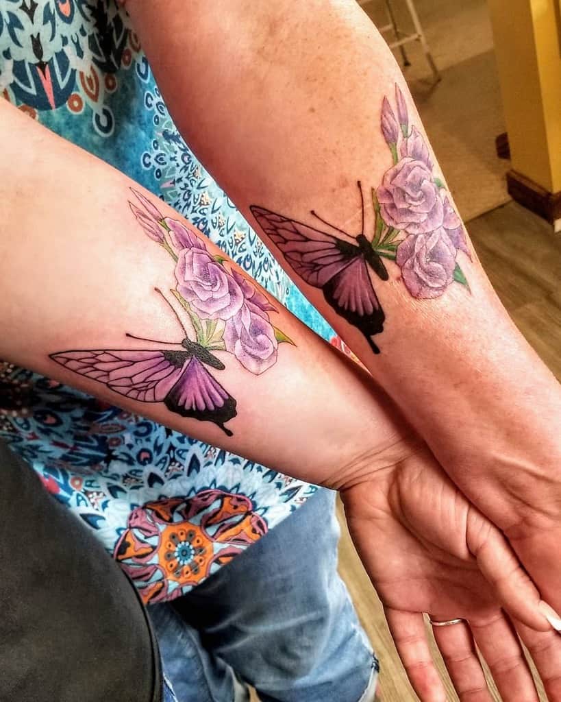 Matching butterfly and purple rose tattoos on forearms, featuring bold black wings and soft floral details for a meaningful design.