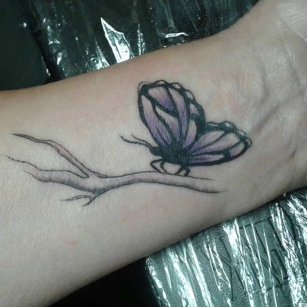 A tattoo of a purple butterfly sitting on a branch on a wrist