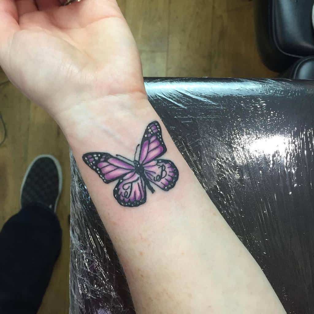 A purple butterfly tattoo on a person's wrist with initials on its wings