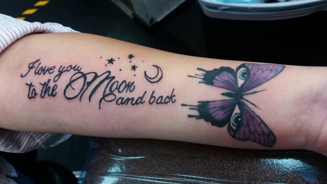 Tattooed arm with "I love you to the moon and back" and a purple butterfly with stars and moon