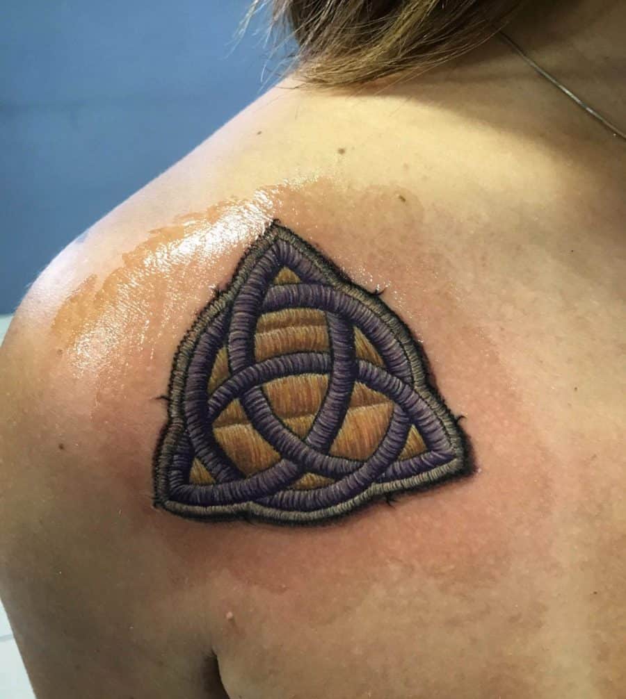 Textile-effect tattoo of an interwoven Celtic knot, created with realistic stitched elements and a handcrafted look.