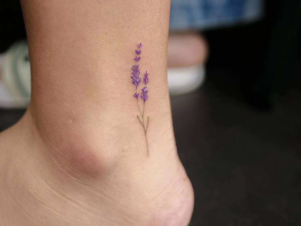 A small lavender tattoo is inked on the inner ankle, showcasing delicate purple flowers and vibrant green stems