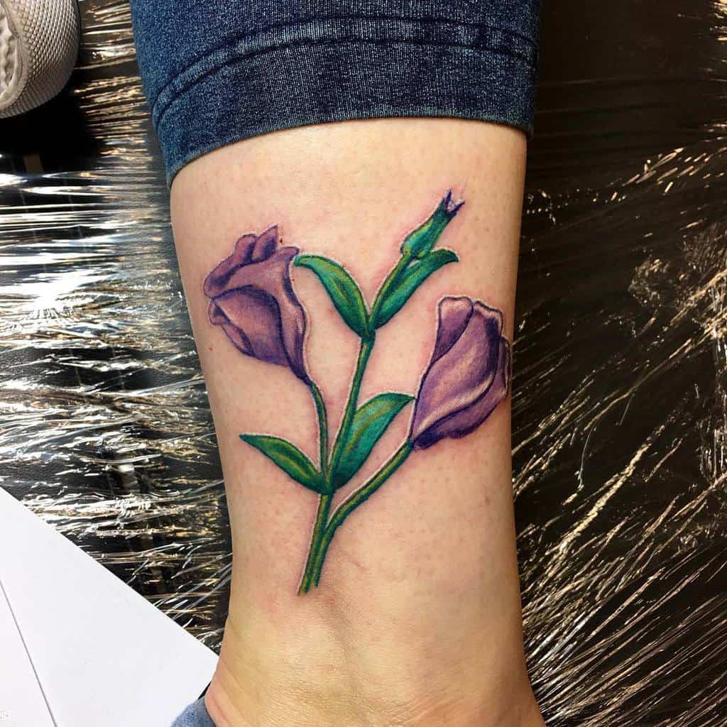 Purple flower tattoo with vibrant blooms and lush green on the lower leg