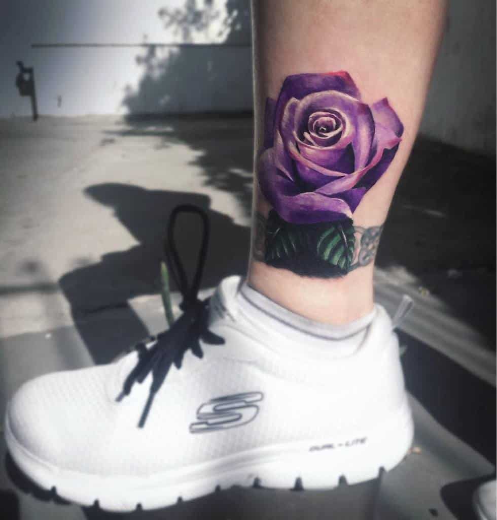 Realistic purple rose ankle tattoo with green leaves, featuring detailed shading and vibrant colors, placed above the ankle