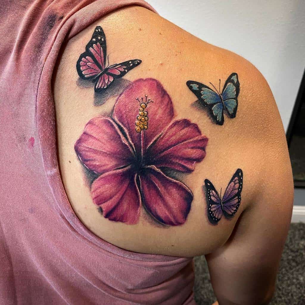 A vibrant tattoo of a pink hibiscus flower with a hint of purple, adorned by three butterflies, graces a shoulder
