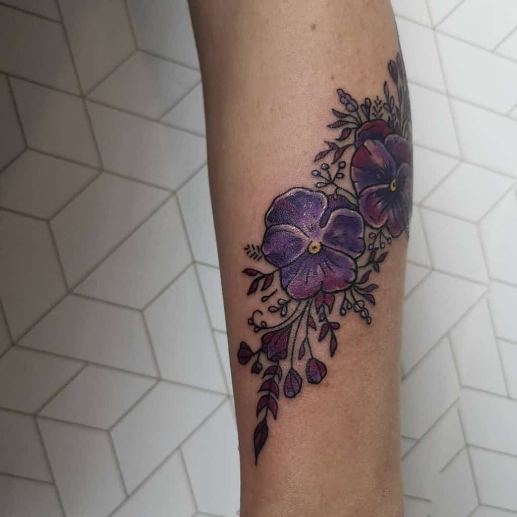 Forearm tattoo of two striking purple flowers with lush leaves