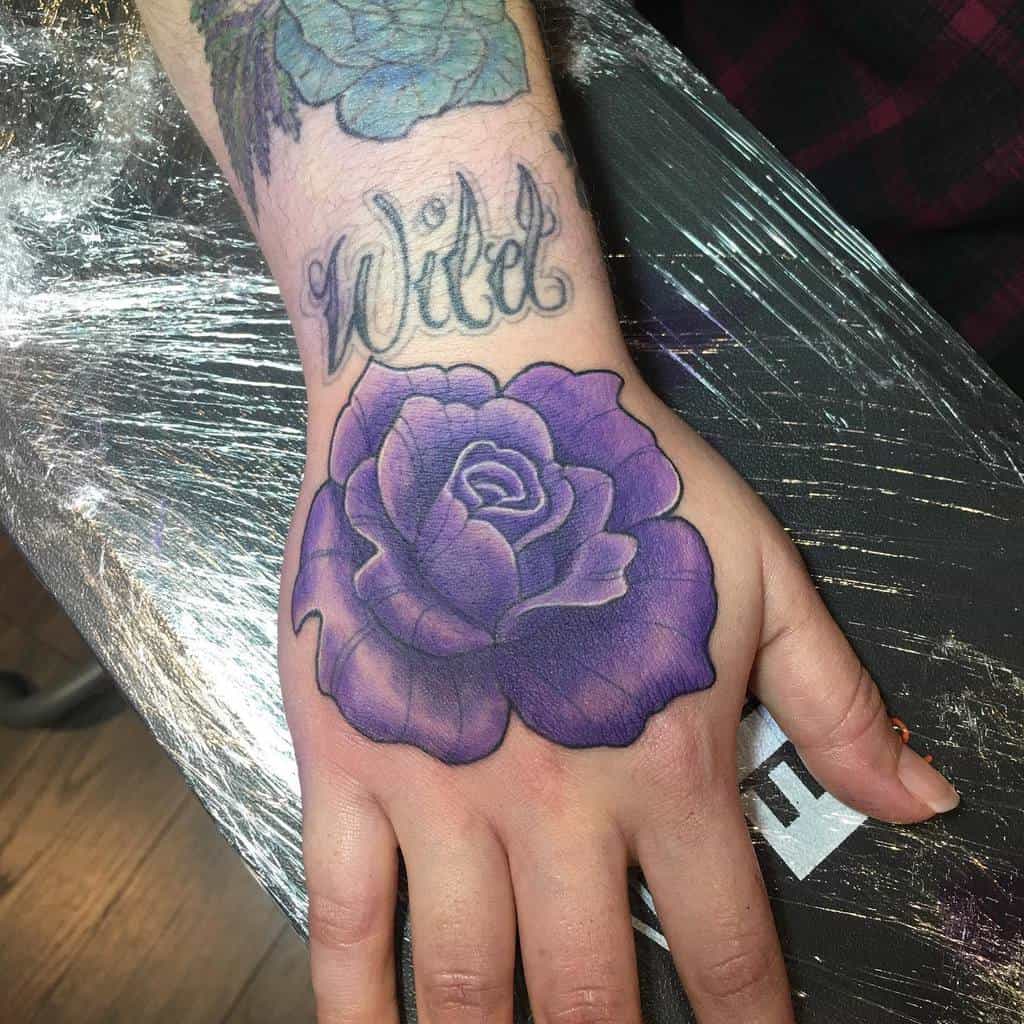 A hand adorned with a striking purple rose tattoo and the word "wild" elegantly scripted above
