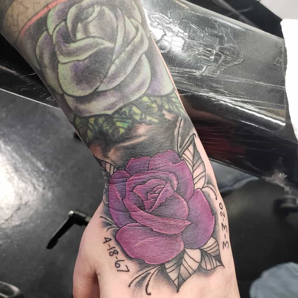 A vibrant purple rose tattoo with lush green leaves adorns a hand
