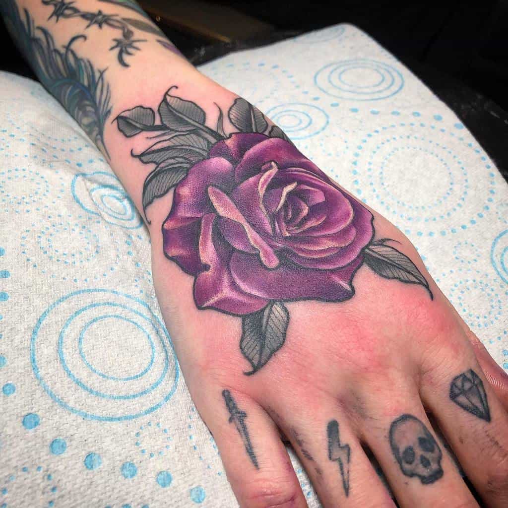 A hand adorned with a purple rose tattoo graces the back, encircled by inky black leaves