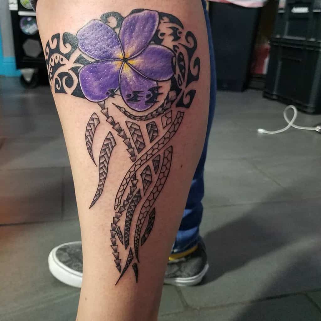 Tribal-inspired leg tattoo featuring a vibrant purple flower with intricate black patterns and geometric elements