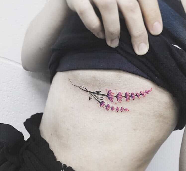 A delicate lavender tattoo in shades of purple and pink adorns a person's ribcage