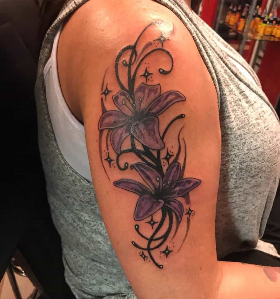 Tattoo of vibrant purple lilies with swirls and stars on an upper arm