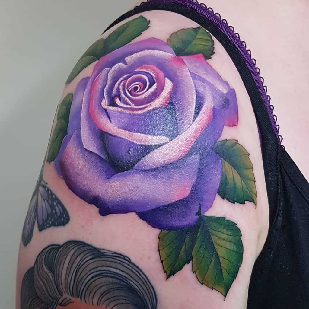 Purple rose tattoo on upper arm, with green leaves