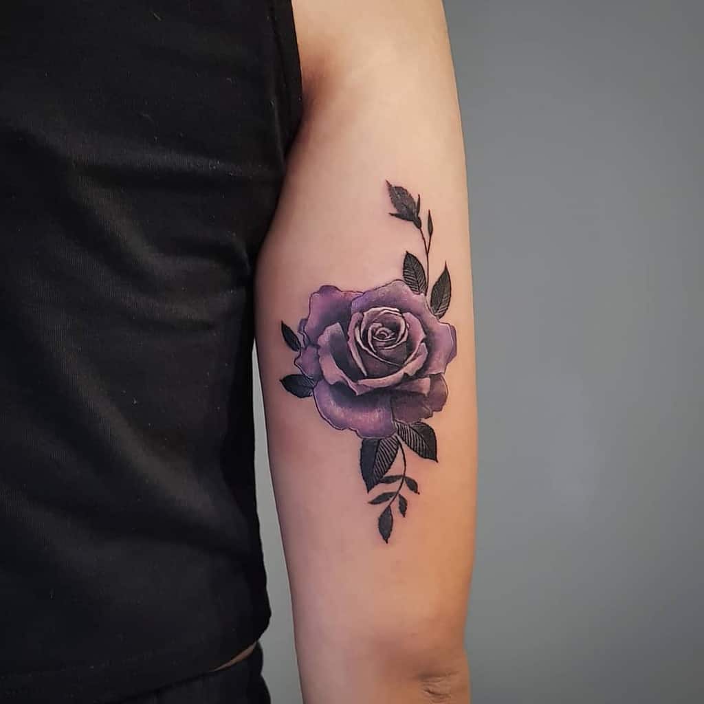 A purple rose tattoo with leaves on an upper arm