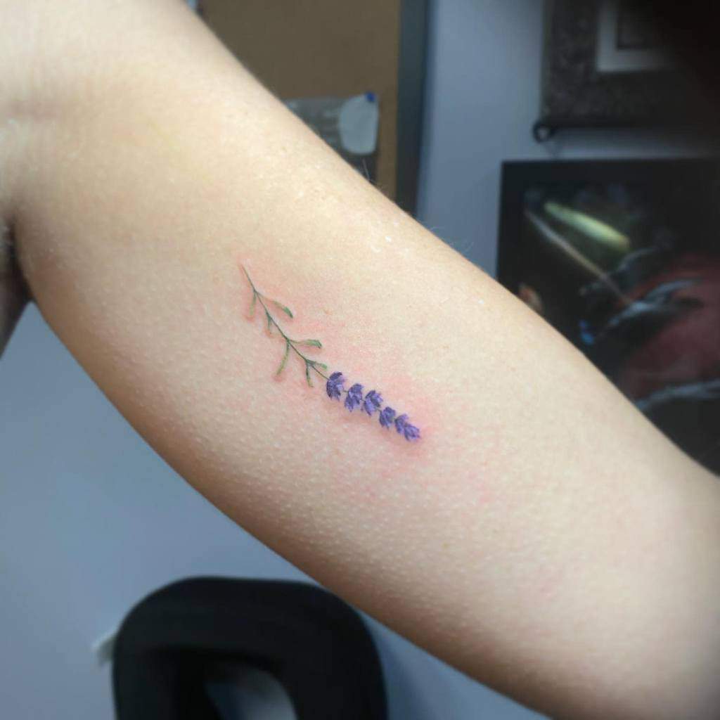 Minimalistic tattoo of a lavender sprig with green leaves and purple flowers on a forearm